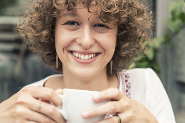 Porträt einer lächelnden jungen Frau mit einer Tasse Kaffee - TAMF000635