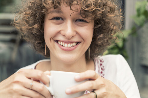 Porträt einer lächelnden jungen Frau mit einer Tasse Kaffee - TAMF000635