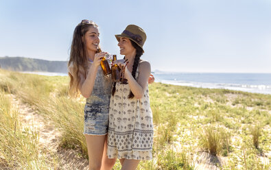 Two friends toasting with beer bottles on the beach - MGOF002371