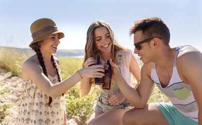 Drei Freunde stoßen mit Bierflaschen am Strand an - MGOF002376