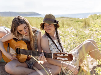 Teenager-Mädchen spielt Gitarre für ihre Freunde am Strand - MGOF002380