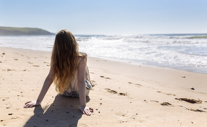 Rückenansicht eines am Strand sitzenden Mädchens im Teenageralter - MGOF002391
