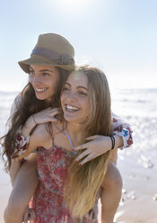 Happy teenage girl giving her best friend a piggyback ride on the beach - MGOF002406