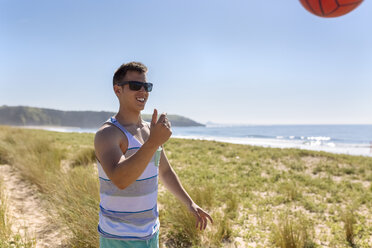 Lächelnder junger Mann spielt mit Ball am Strand - MGOF002415