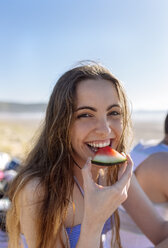 Porträt eines lächelnden Teenagers, der am Strand eine Wassermelone isst - MGOF002418
