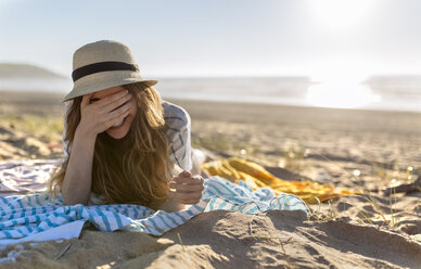 Porträt eines lächelnden Teenagers, der am Strand liegt und sein Gesicht mit der Hand bedeckt - MGOF002424