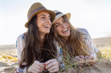 Portrait of two best friends with summer hats lying on the beach - MGOF002430