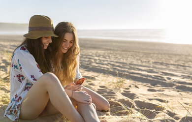 Two best friends sitting on the beach looking at smartphone - MGOF002432