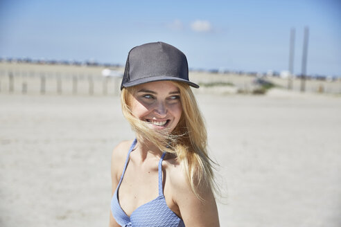Glückliche junge Frau mit Baseballmütze am Strand - SRYF000047