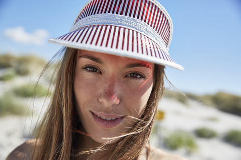 Porträt einer lächelnden jungen Frau mit Sonnenblende am Strand, lizenzfreies Stockfoto