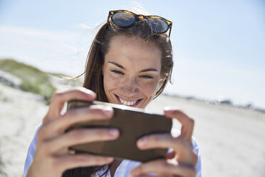 Lächelnde junge Frau mit Handy am Strand - SRYF000069