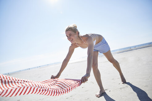 Junge Frau breitet ihr Handtuch am Strand aus - SRYF000072