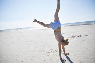 Young woman doing a handstand on the beach - SRYF000073