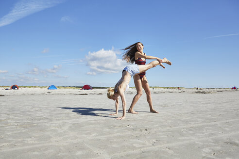Young woman helping friend doing a handstand on the beach - SRYF000075