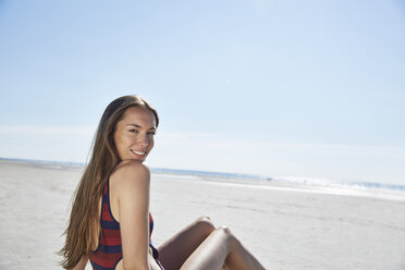 Lächelnde junge Frau am Strand sitzend - SRYF000079