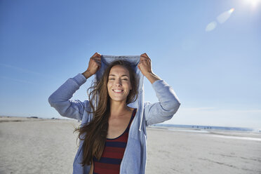 Lächelnde junge Frau mit Kapuzenpulli am Strand - SRYF000083