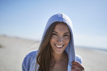 Lächelnde junge Frau mit Kapuzenpulli am Strand - SRYF000084