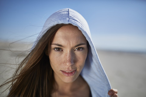 Lächelnde junge Frau mit Kapuzenpulli am Strand, lizenzfreies Stockfoto