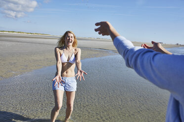 Glückliche junge Frau, die am Strand mit Wasser bespritzt wird - SRYF000097