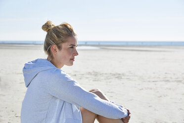 Young woman wearing hoodie sitting on the beach - SRYF000109