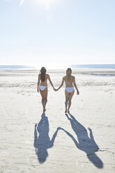 Zwei Freundinnen im Bikini gehen Hand in Hand am Strand - SRYF000129