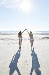 Two female friends in bikini walking hand in hand on the beach - SRYF000130