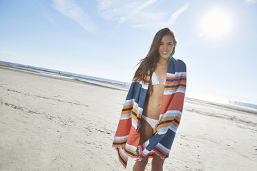 Lächelnde junge Frau im Bikini mit Decke am Strand - SRYF000136