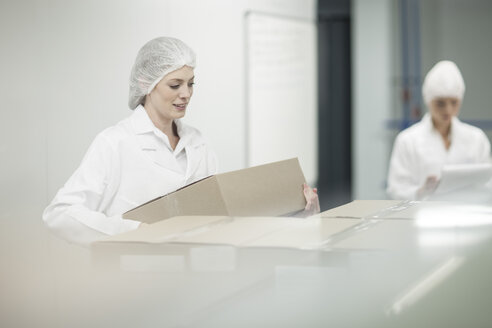 Woman in protective workwear lifting cardboard box - ZEF010092