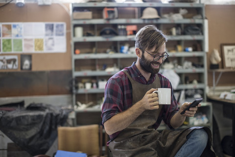 Mann mit Mobiltelefon in der Kaffeepause in der Werkstatt, lizenzfreies Stockfoto
