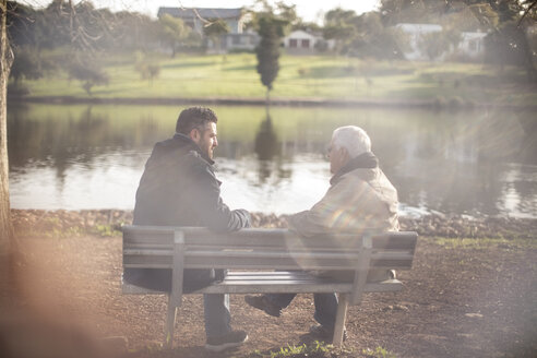 Senior man and adult son sitting on a bench talking - ZEF010189