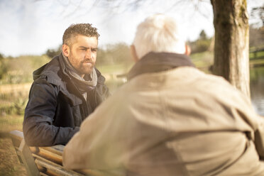 Senior man and adult son sitting on a bench talking - ZEF010191