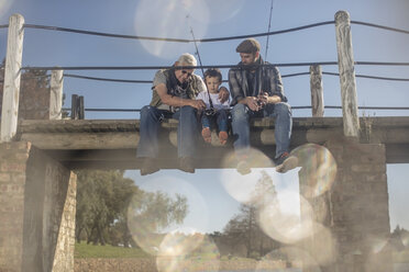 Grandfather, father and son sitting on a bridge fishing together - ZEF010221