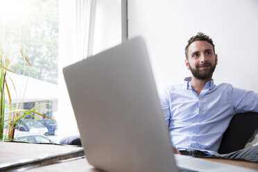 Young man with laptop at the window - WESTF021649