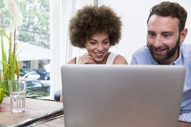 Young woman and man using laptop at the window - WESTF021653