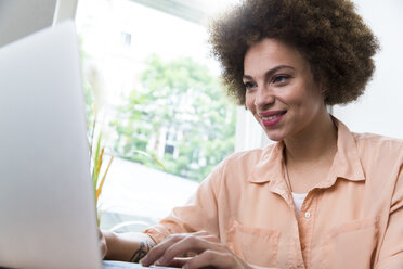 Smiling young woman using laptop at the window - WESTF021655