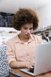 Junge Frau mit Laptop in einem Café - WESTF021659