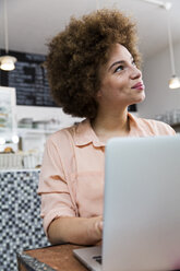 Smiling young woman with laptop in a cafe looking up - WESTF021660