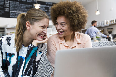 Zwei glückliche junge Frauen mit Laptop in einem Cafe - WESTF021664