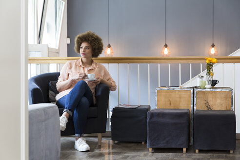 Junge Frau sitzt in einem Sessel in einem Cafe - WESTF021671