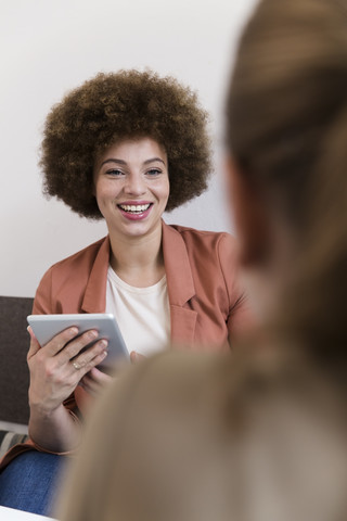 Lächelnde junge Frau mit Tablet in einem Café und Blick auf eine Frau, lizenzfreies Stockfoto