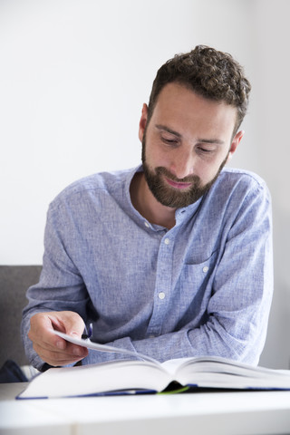 Junger Mann liest ein Buch am Tisch, lizenzfreies Stockfoto