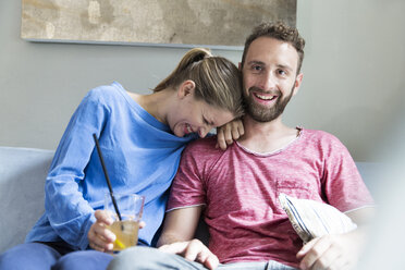 Happy young couple sitting on couch with drink - WESTF021698