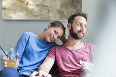 Smiling young couple sitting on couch with drink - WESTF021699