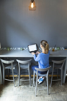 Junge Frau sitzt auf einem Barhocker und benutzt einen Laptop - WESTF021705