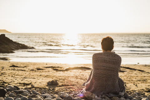 Frankreich, Halbinsel Crozon, reife Frau sitzt bei Sonnenuntergang am Strand, lizenzfreies Stockfoto