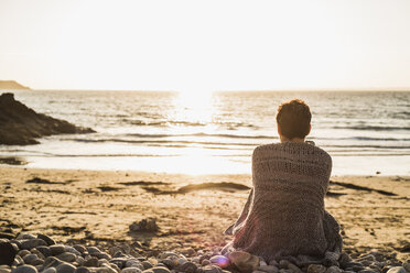 France, Crozon peninsula, mature woman sitting on beach at sunset - UUF008324