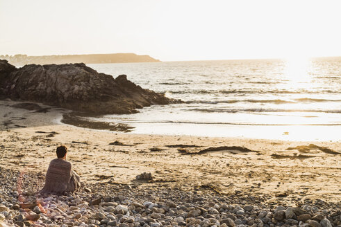 Frankreich, Halbinsel Crozon, Frau sitzt bei Sonnenuntergang am Strand - UUF008325