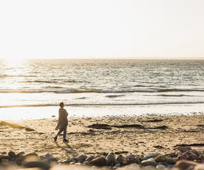 Frankreich, Halbinsel Crozon, Frau geht bei Sonnenuntergang am Strand spazieren - UUF008327