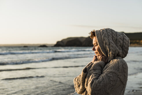 Frankreich, Halbinsel Crozon, Frau in Strickjacke am Strand bei Sonnenuntergang - UUF008329