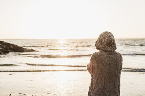 Frankreich, Halbinsel Crozon, Frau in Strickjacke am Strand bei Sonnenuntergang - UUF008331